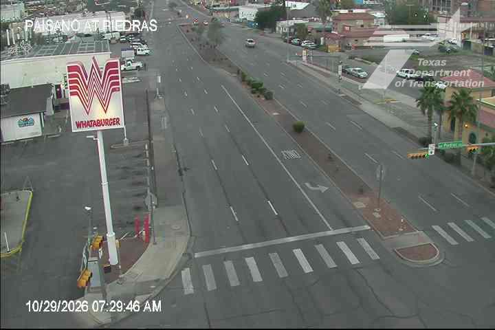 A wide, multi-lane road with light traffic flows through an urban area, featuring a prominent Whataburger sign and a crosswalk at an intersection with traffic signals.