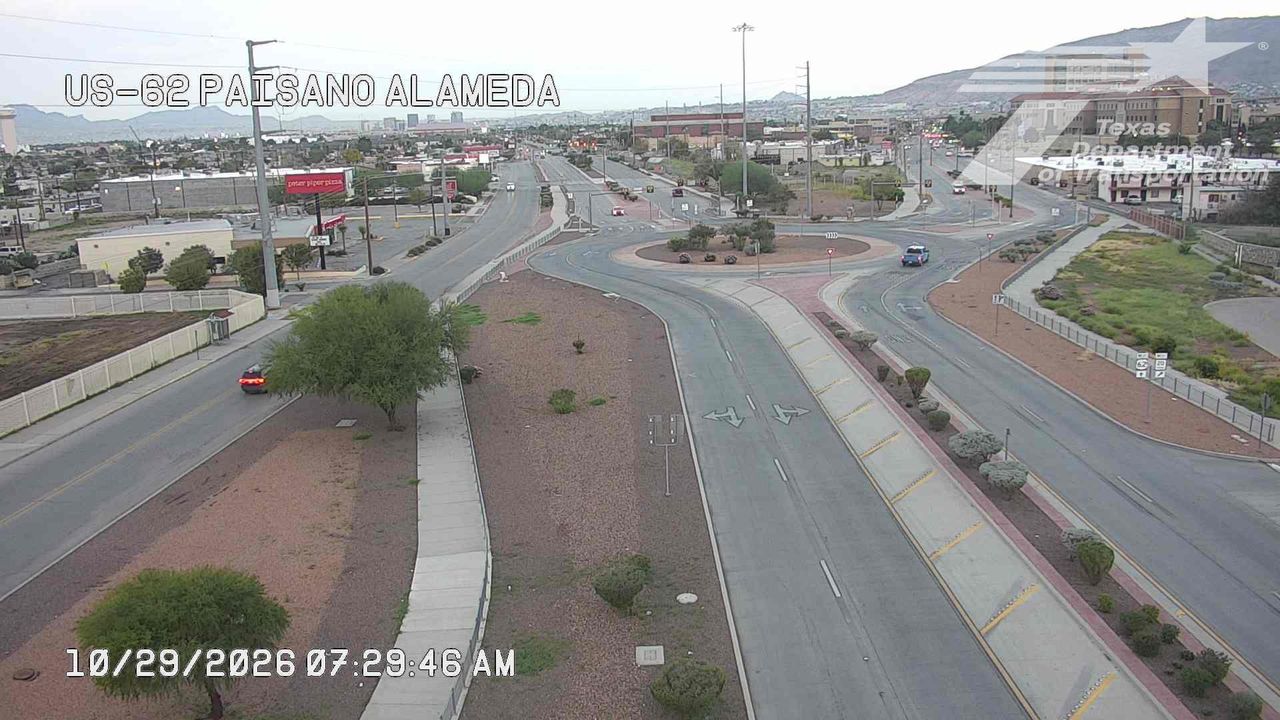 A wide view of a multi-lane intersection with light traffic, featuring a roundabout and commercial buildings under an overcast sky.