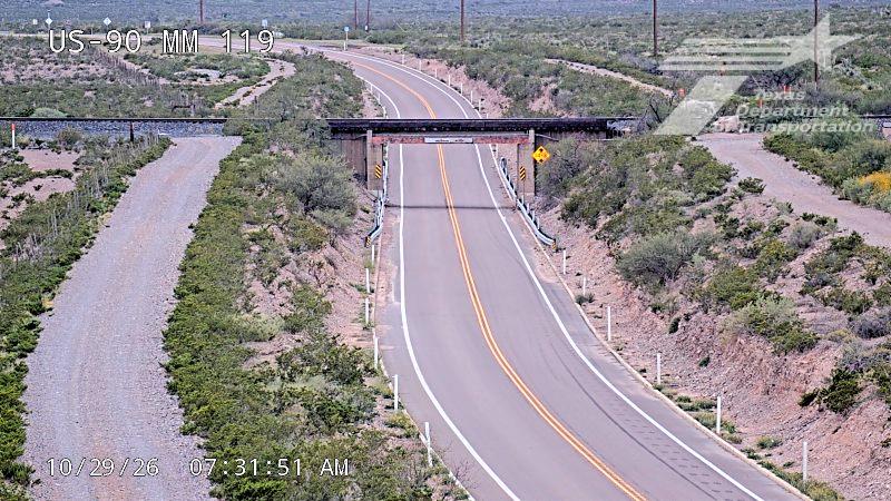 Empty highway with no vehicles, passing under an overpass in a dry, brush-covered landscape.